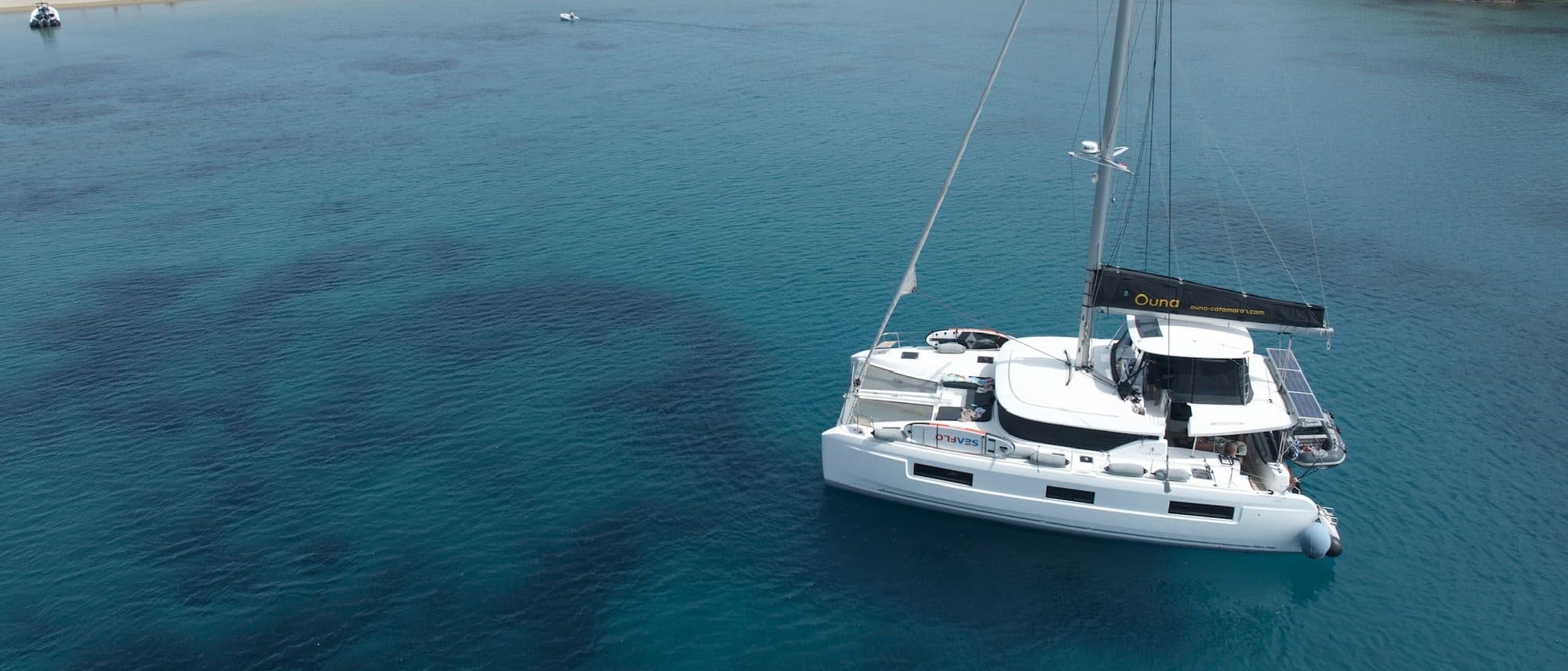 Ouna anchored alone in a deep blue Cycladic cove, drone view