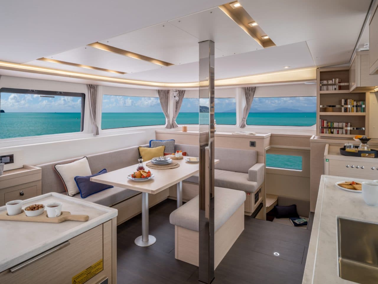Interior saloon with dining table, bench seating, and panoramic sea view through curved windows