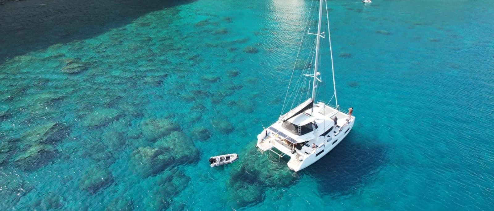 Ouna anchored alone in crystal-clear water over a Cycladic reef