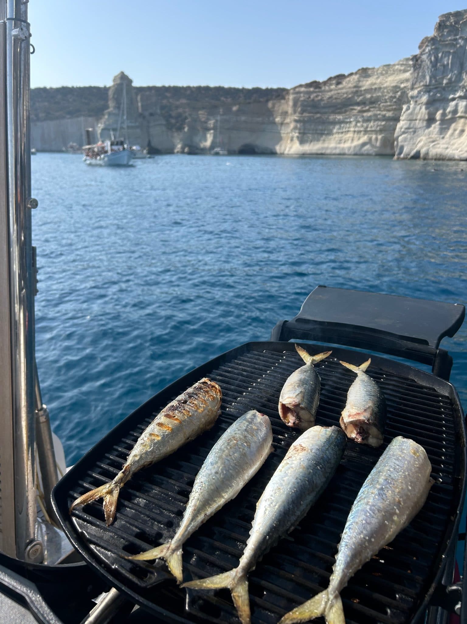 Fresh fish grilling on the boat's BBQ with white Milos cliffs in the background