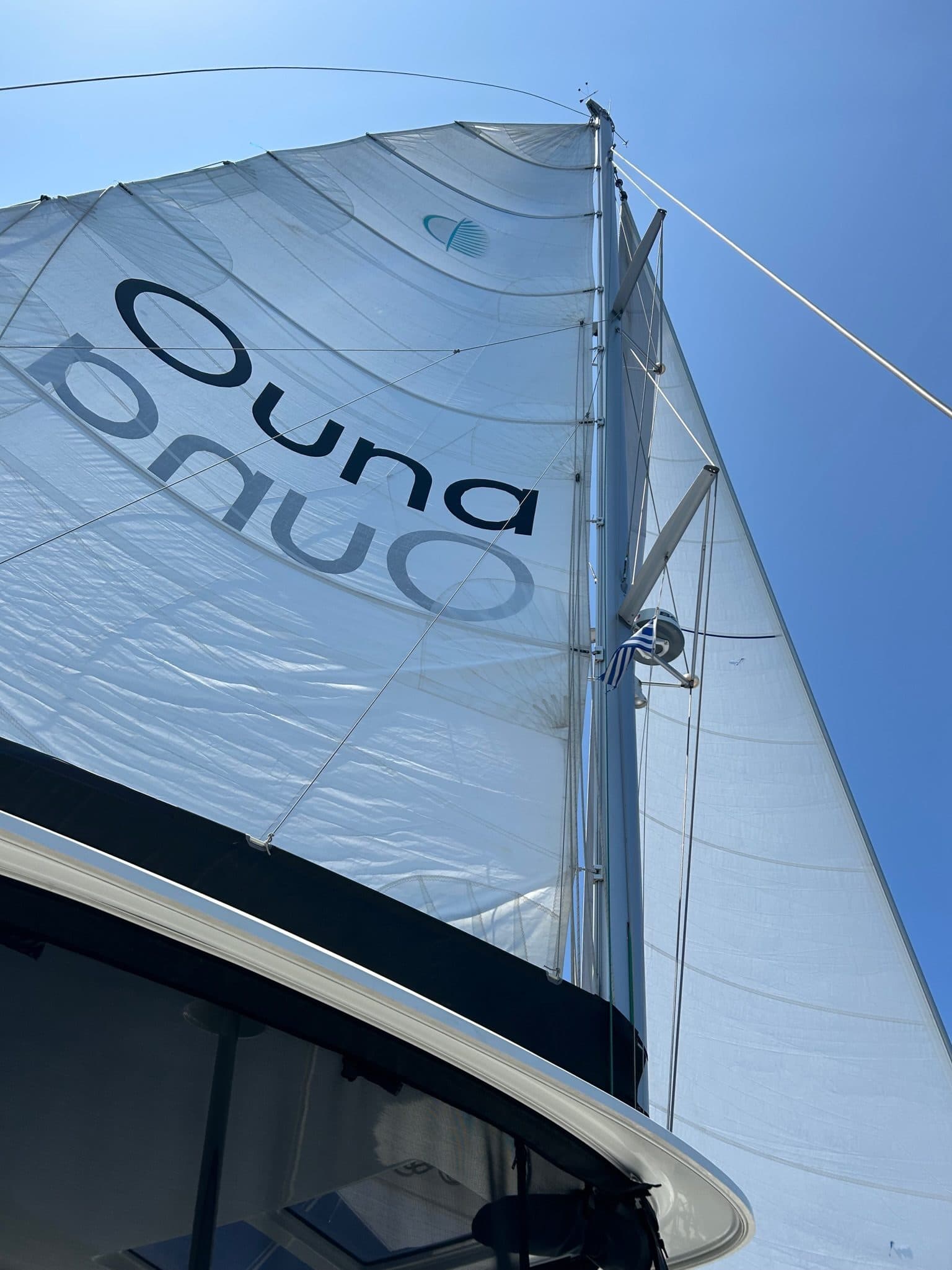 Ouna under sail, branded mainsail full against a blue sky