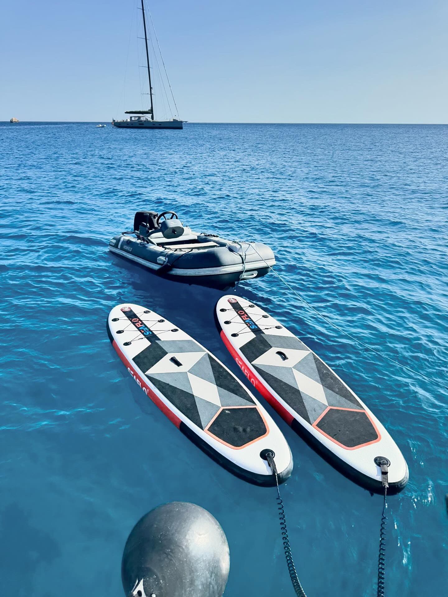 Stand-up paddleboards floating next to Ouna at anchor in deep blue water